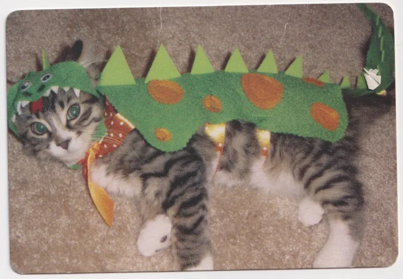 A silly photo of a cat in a dinosaur costume laying on some carpet.